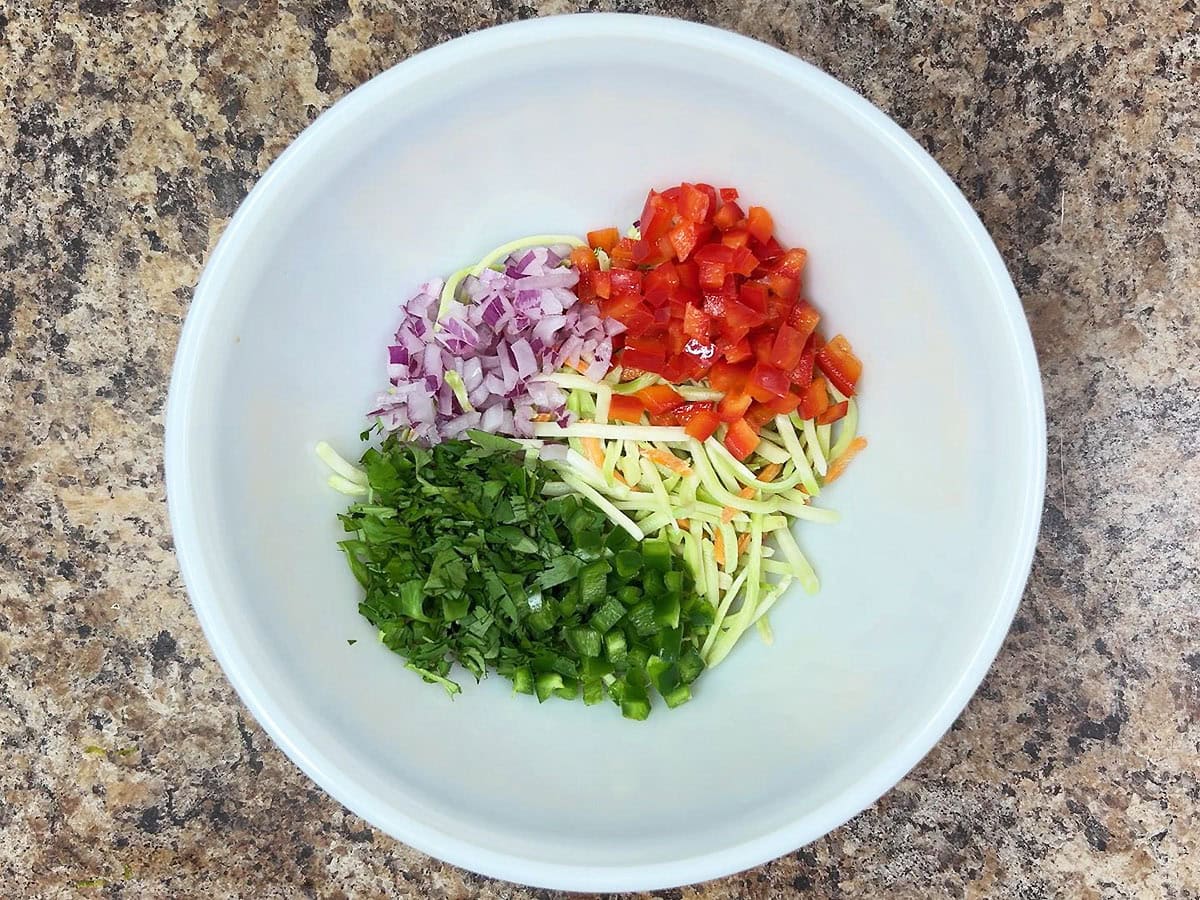Coleslaw mix, diced red bell pepper, diced red onion, chopped cilantro, and diced green bell pepper in a mixing bowl.