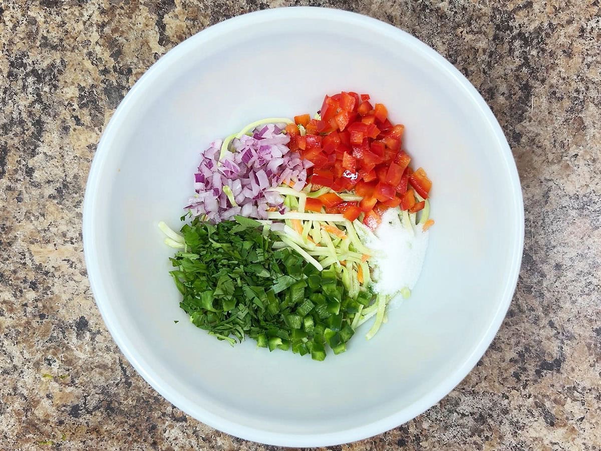 Coleslaw mix, diced red bell pepper, diced red onion, chopped cilantro, diced green bell pepper, and salt in a mixing bowl.