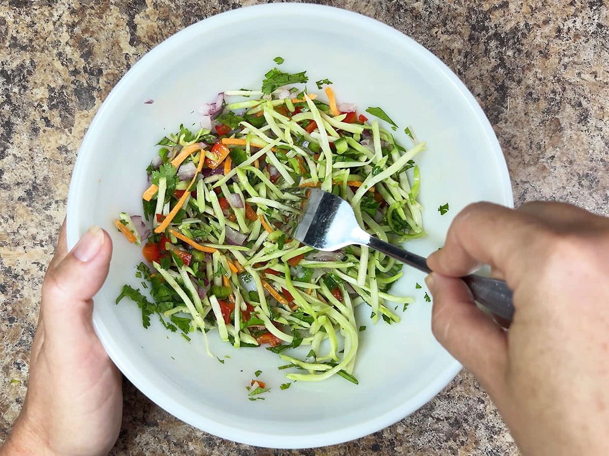 Hands mixing the slaw ingredients together with a fork.