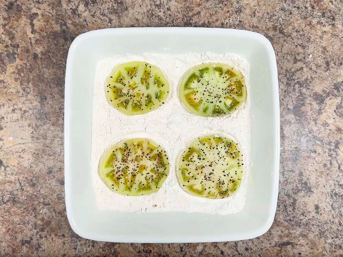 Coating sliced green tomatoes in flour.
