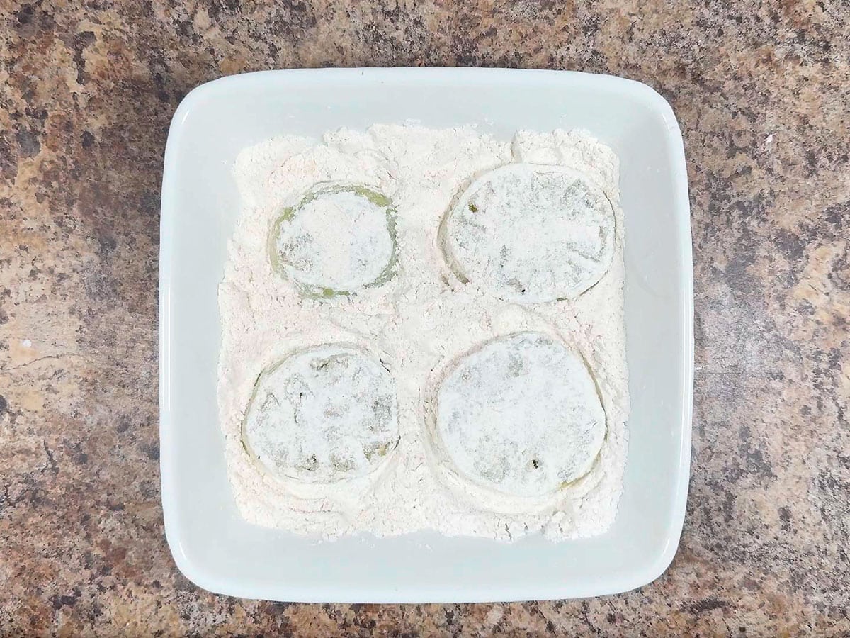 Coating both sides of sliced green tomatoes in flour.