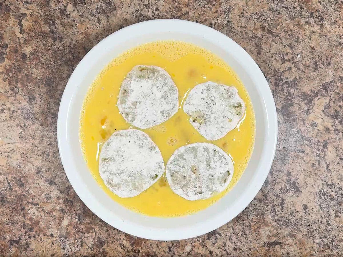 Coating flour coated sliced tomatoes in an egg mixture.