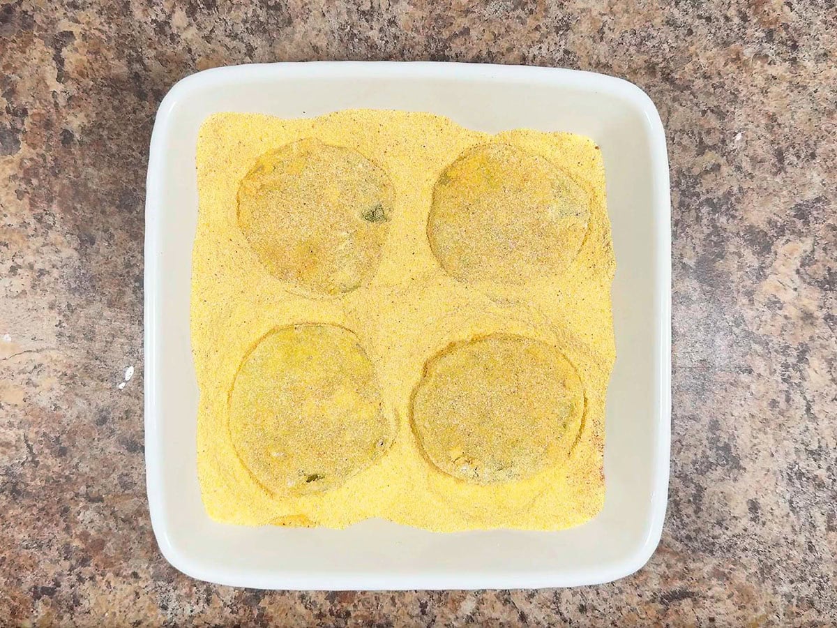 Coating both sides of green tomato slices in cornmeal.