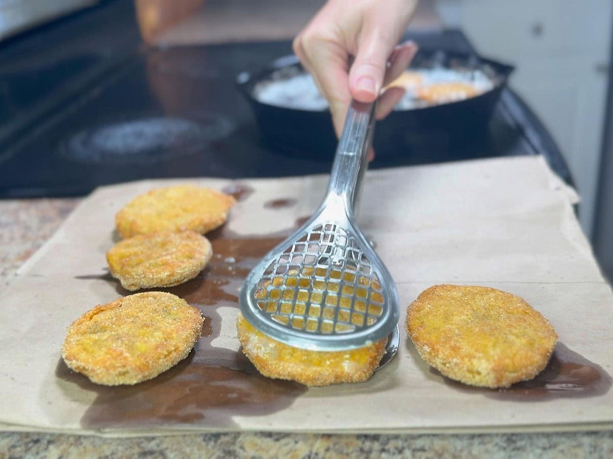 Removing the fried green tomatoes from the hot oil to a paper sack to drain.