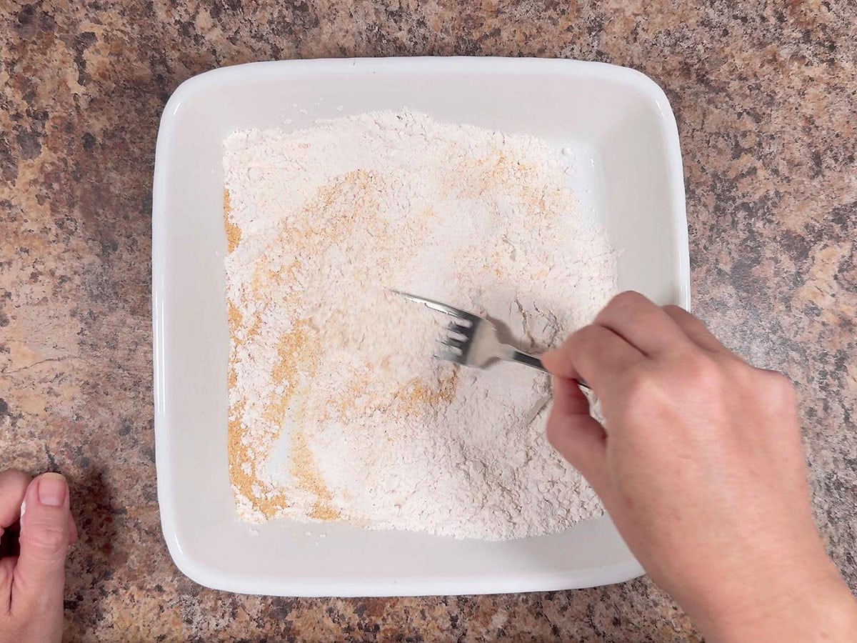 Whisking together flour and garlic powder in a shallow dish.