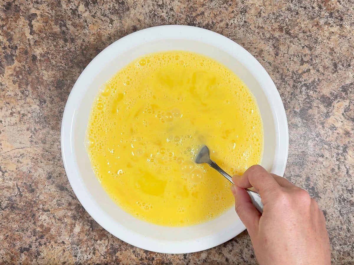 Whisking together eggs and milk in a shallow dish.