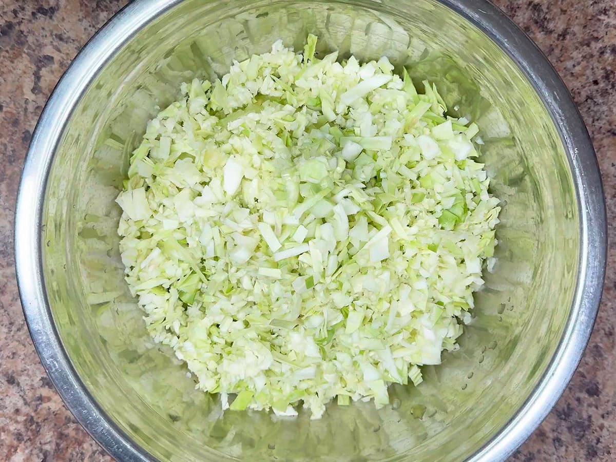 Shredded green cabbage added to the diced green tomatoes in a metal mixing bowl.
