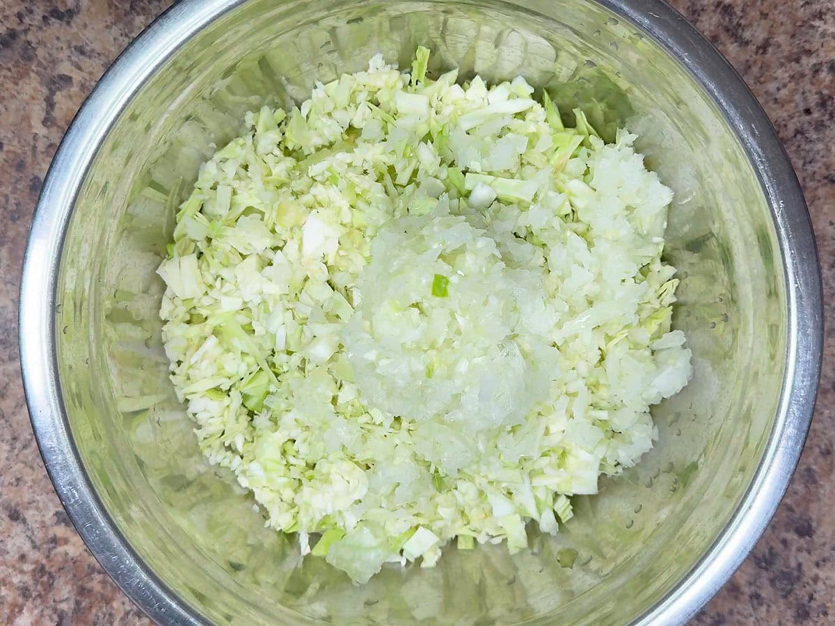 Diced onions added to the shredded green cabbage and diced green tomatoes in a metal mixing bowl.