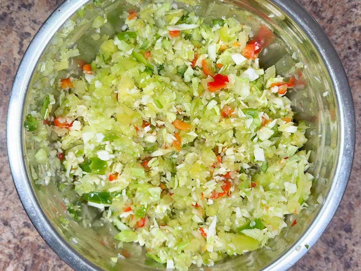 Salted chopped vegetables in a metal mixing bowl.