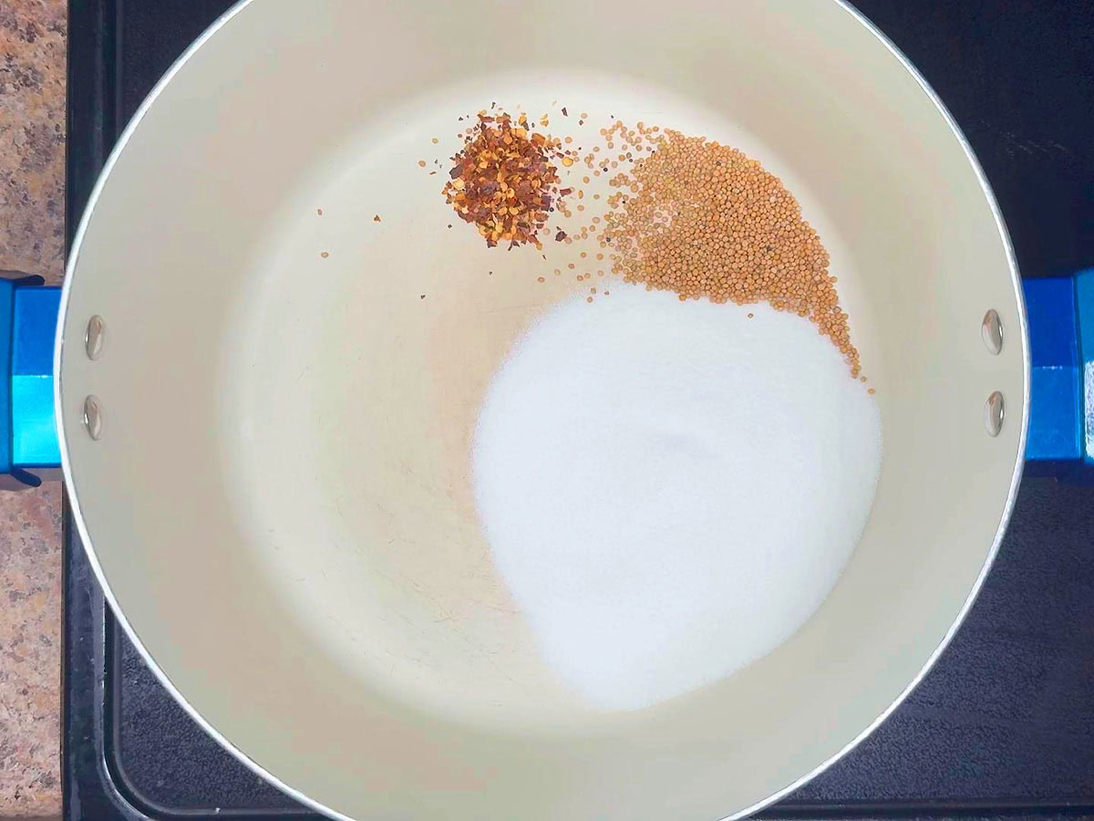 Red pepper flakes added to the mustard seeds and sugar in a stockpot.
