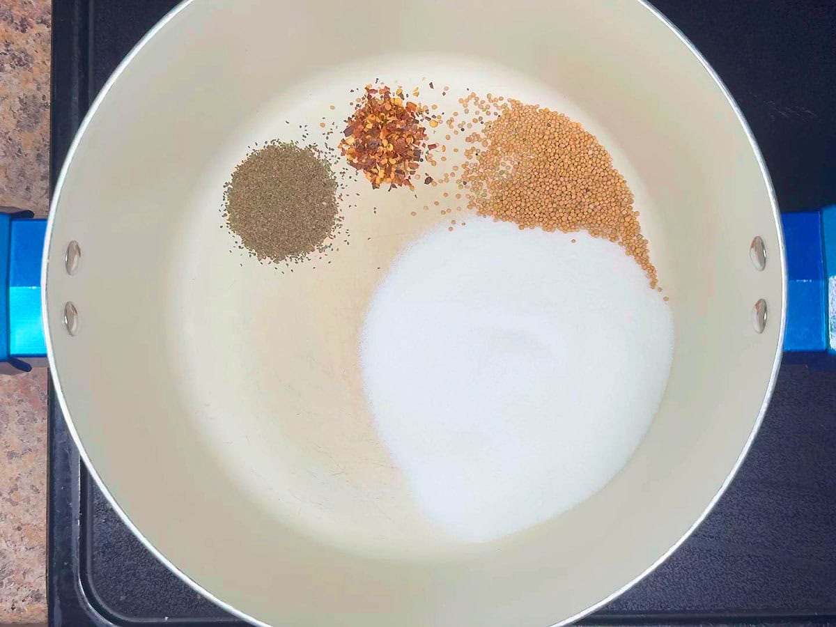 Celery seed added to red pepper flakes, mustard seeds, and sugar in a stockpot.