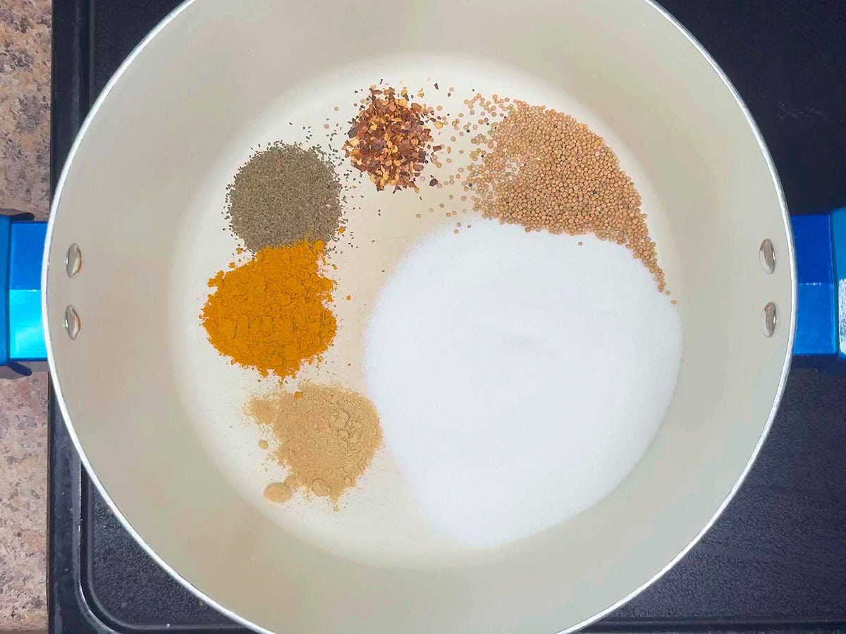 Ground ginger added to celery seed, red pepper flakes, mustard seeds, and sugar in a stockpot.