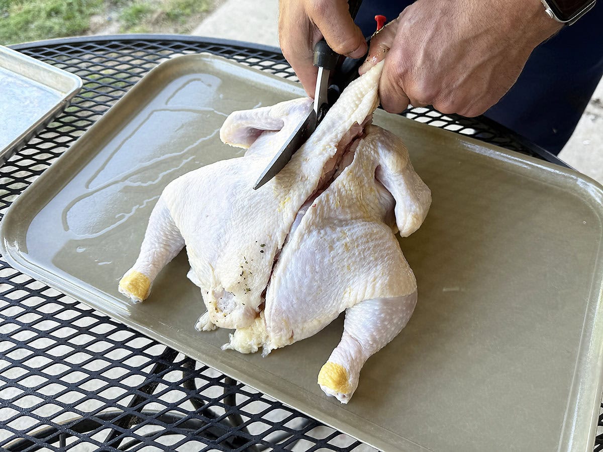 Using kitchen shears to cut up the other side of the chicken's backbone.