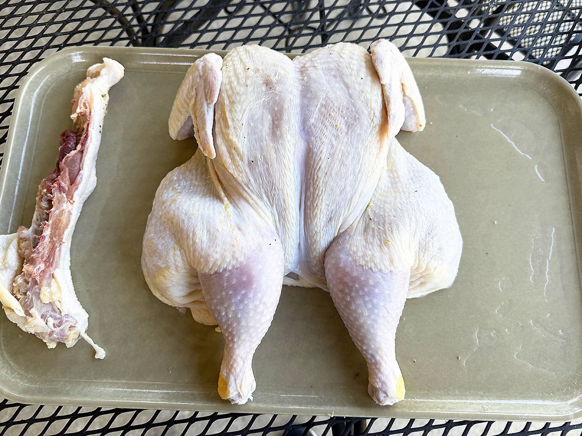 Flattened chicken on a large cutting board with the backbone removed.