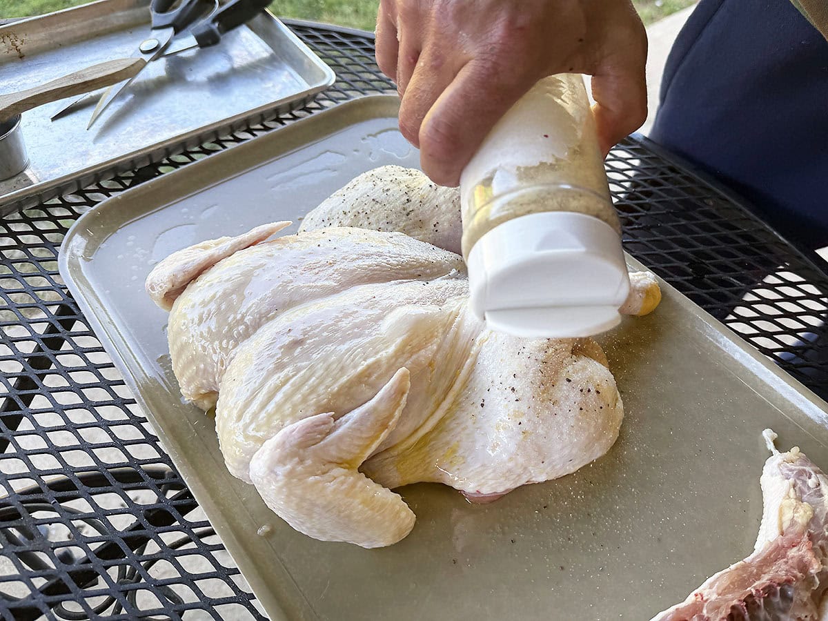 Sprinkling the outside of a spatchcocked chicken with seasoning.