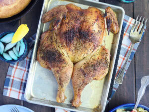 Smoked spatchcock chicken on a tray with a skillet of cornbread, a bowl of pasta salad, and glasses of sweet tea on the side