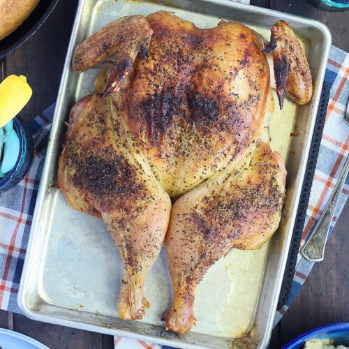 Smoked spatchcock chicken on a tray with a skillet of cornbread, a bowl of pasta salad, and glasses of sweet tea on the side