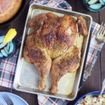 Smoked spatchcock chicken on a tray with a skillet of cornbread, a bowl of pasta salad, and glasses of sweet tea on the side