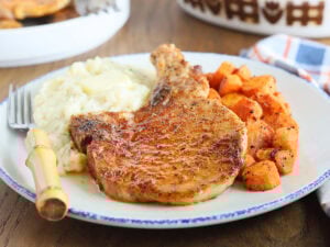 Seasoned air fryer bone in pork chop on a plate with mashed potatoes, roasted carrots and a fork on the side.