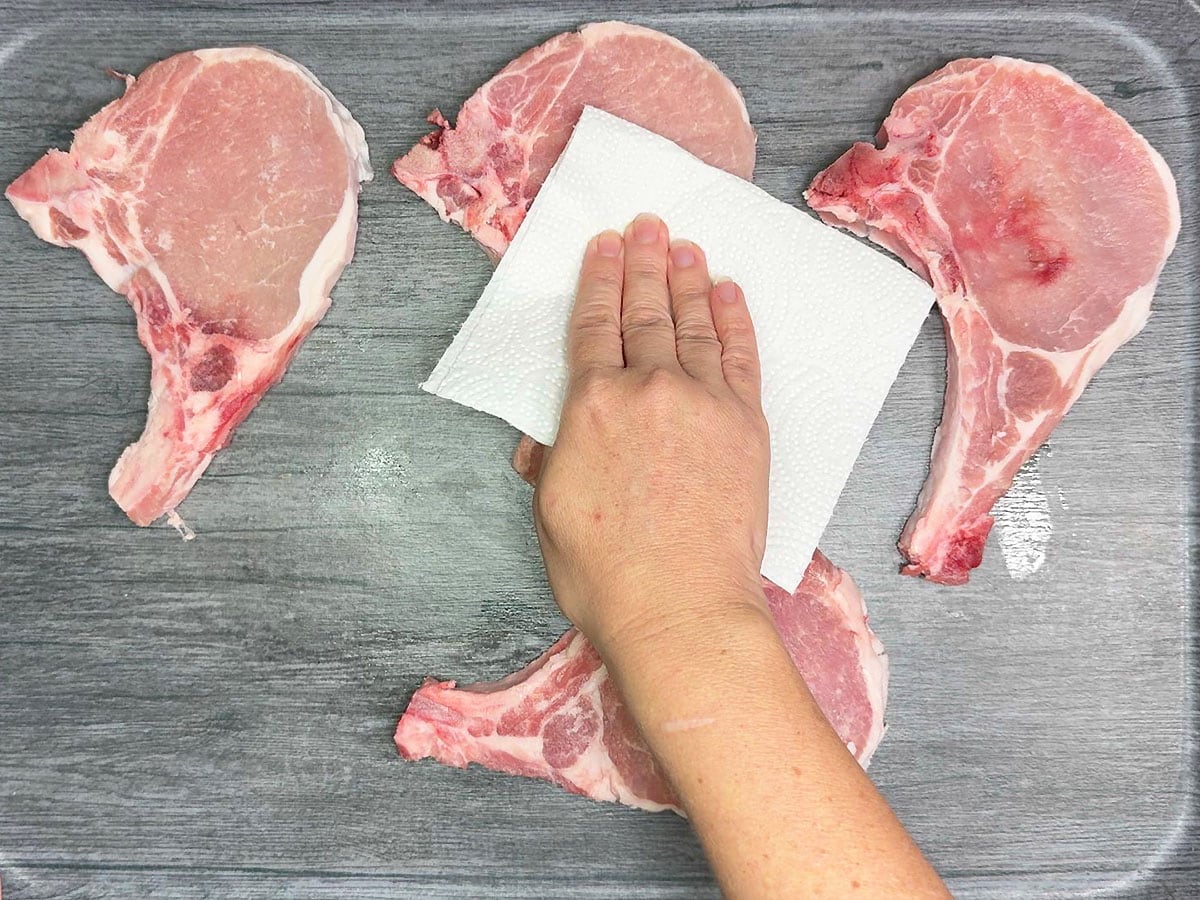 Hand patting the pork chops dry with a paper towel.