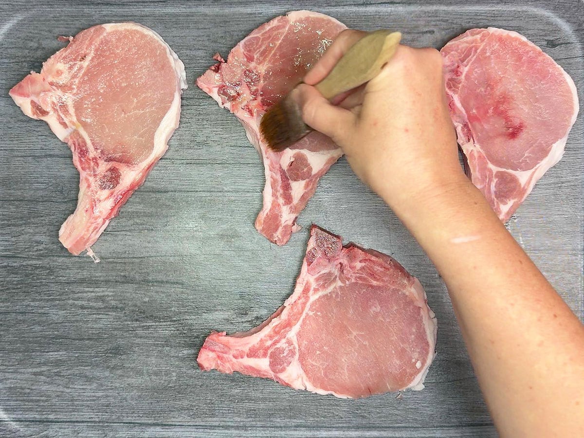 Hand brushing olive oil on the outside of the pork chops.
