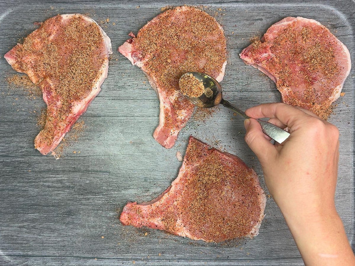 Seasoning the pork chops with the spice rub.