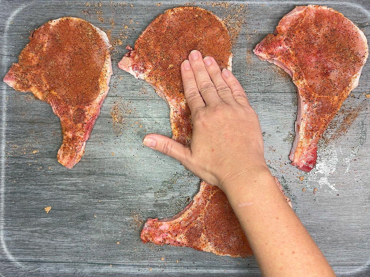 Pressing the spice rub into the pork chops.