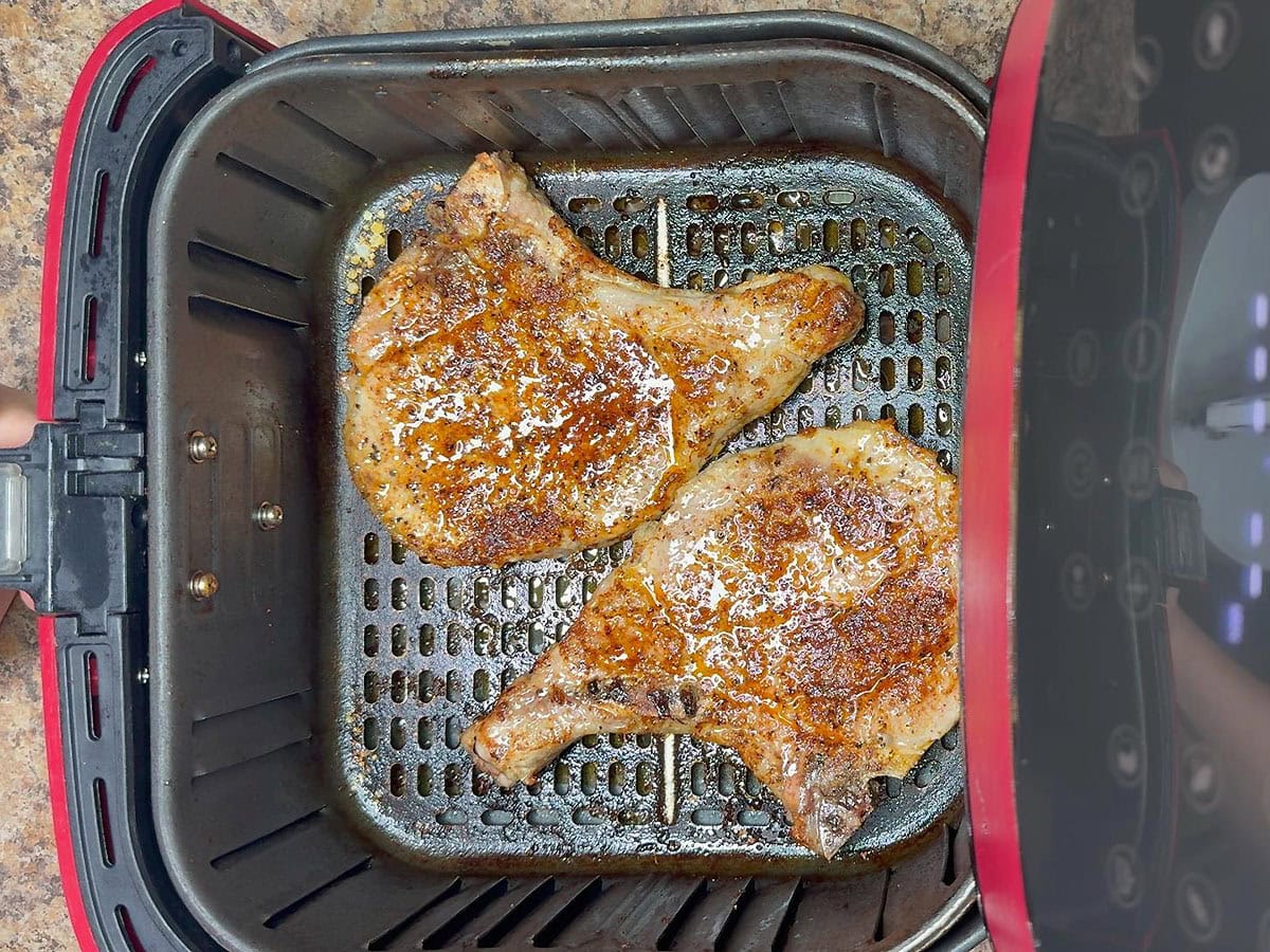 Pork chops in the air fryer after they have cooked for eight minutes.