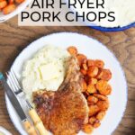 Air fryer bone in pork chop on a plate with mashed potatoes and roasted carrots with a knife and a fork positioned on the side. Serving dishes of potatoes, carrots and additional pork chops can be seen.