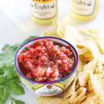 Fresh garden salsa in a decorative bowl, surrounded by tortilla chips and two bottles of Mexican beer in the background.