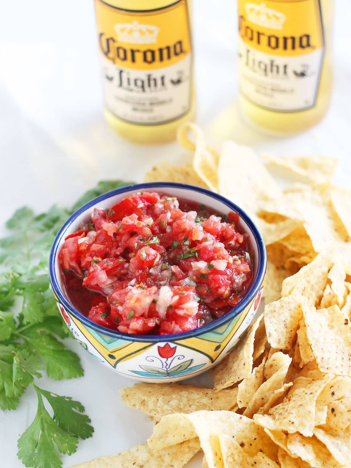 Fresh garden salsa in a decorative bowl, surrounded by tortilla chips and two bottles of Mexican beer in the background.