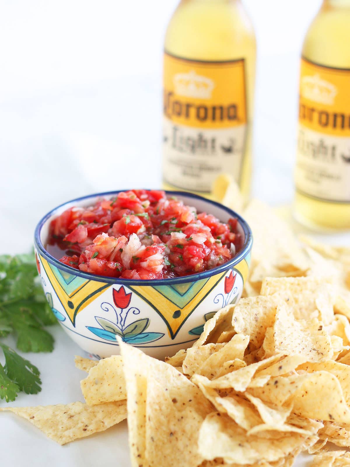 Fresh garden salsa in a decorative bowl, surrounded by tortilla chips and two bottles of Mexican beer in the background.