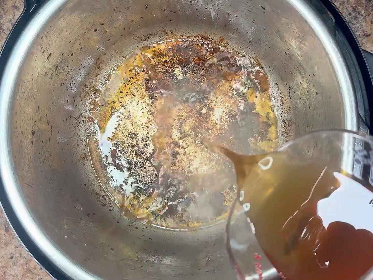 Deglazing the bottom of the Instant Pot with beef broth.