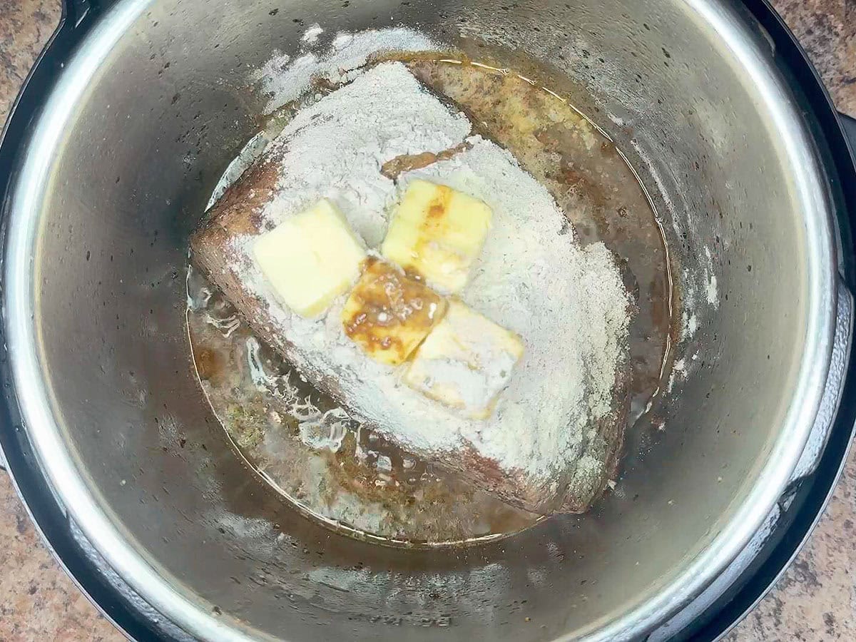 Adding the butter to the roast and seasoning mixes in the Instant Pot.