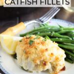 Stuffed catfish fillet on a floral plate with green beans and a lemon wedge. Glass of white wine and a skillet with additional catfish fillets in the background.