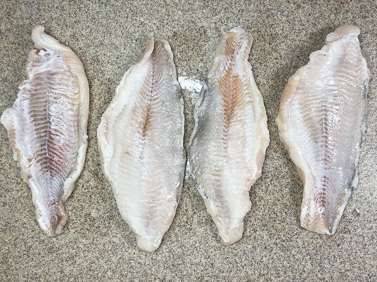 Four catfish fillets flat side up on a cutting board.