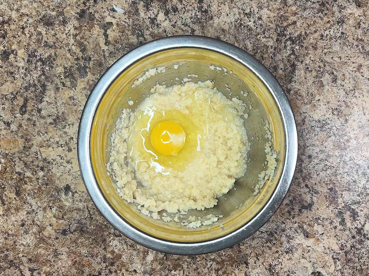 Mashed cornbread and a whole egg in a small mixing bowl.
