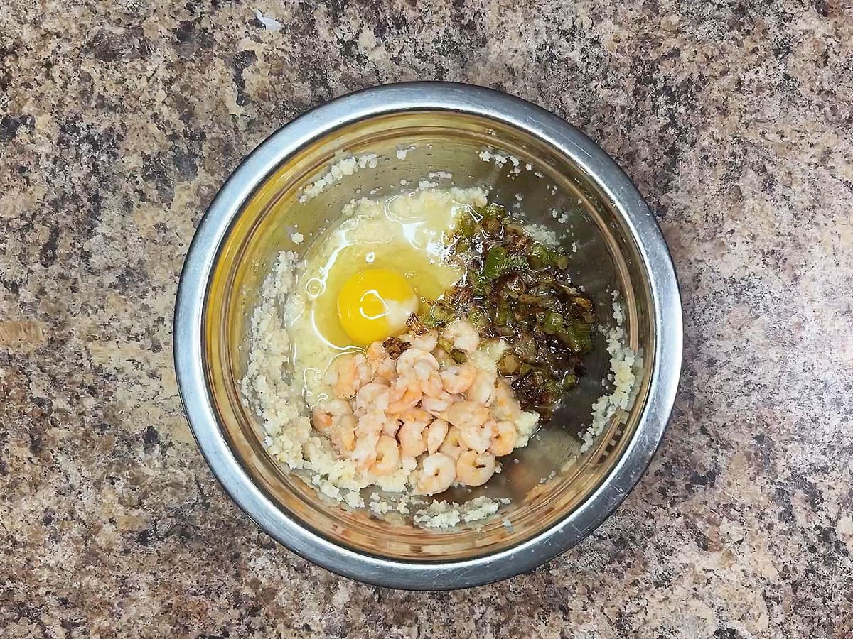 Crumbled cornbread, sauteed veggies, shrimp and whole egg in a small mixing bowl.