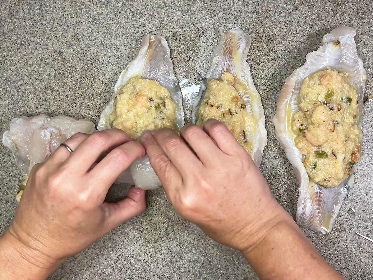 Hands rolling up a catfish fillet around the cornbread and shrimp stuffing.