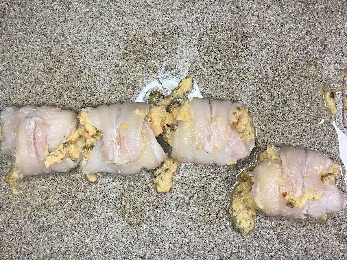Uncooked stuffed and rolled catfish fillets on a cutting board.