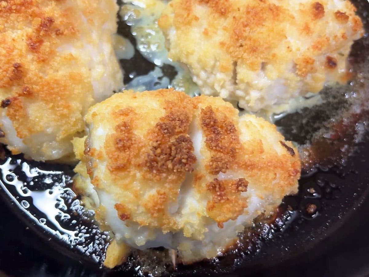 Breaded catfish fillets in a skillet after they have just come out of the oven.