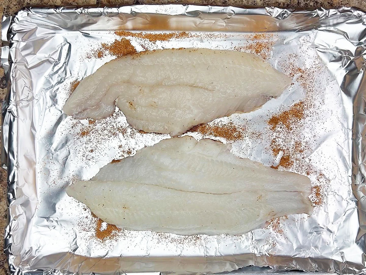 Two catfish fillets on a foil lines baking sheet.