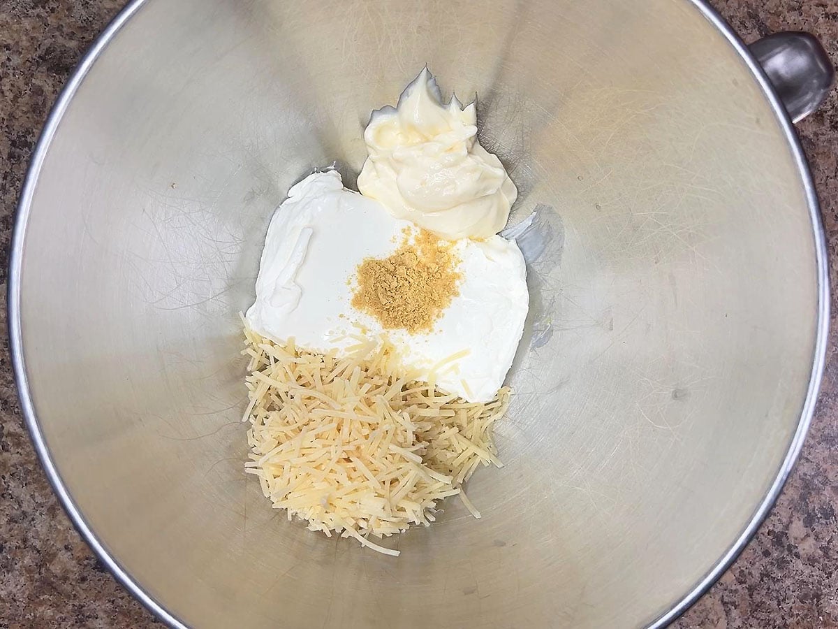 Eight ounces of cream cheese, ¾ cup of shredded Parmesan cheese, mayonnaise, and dried mustard in a mixing bowl.