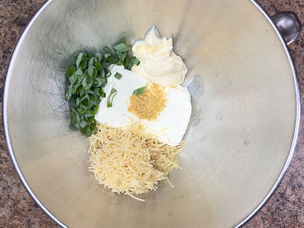 Eight ounces of cream cheese, ¾ cup of shredded Parmesan cheese, mayonnaise, dried mustard, and green onions in a mixing bowl.