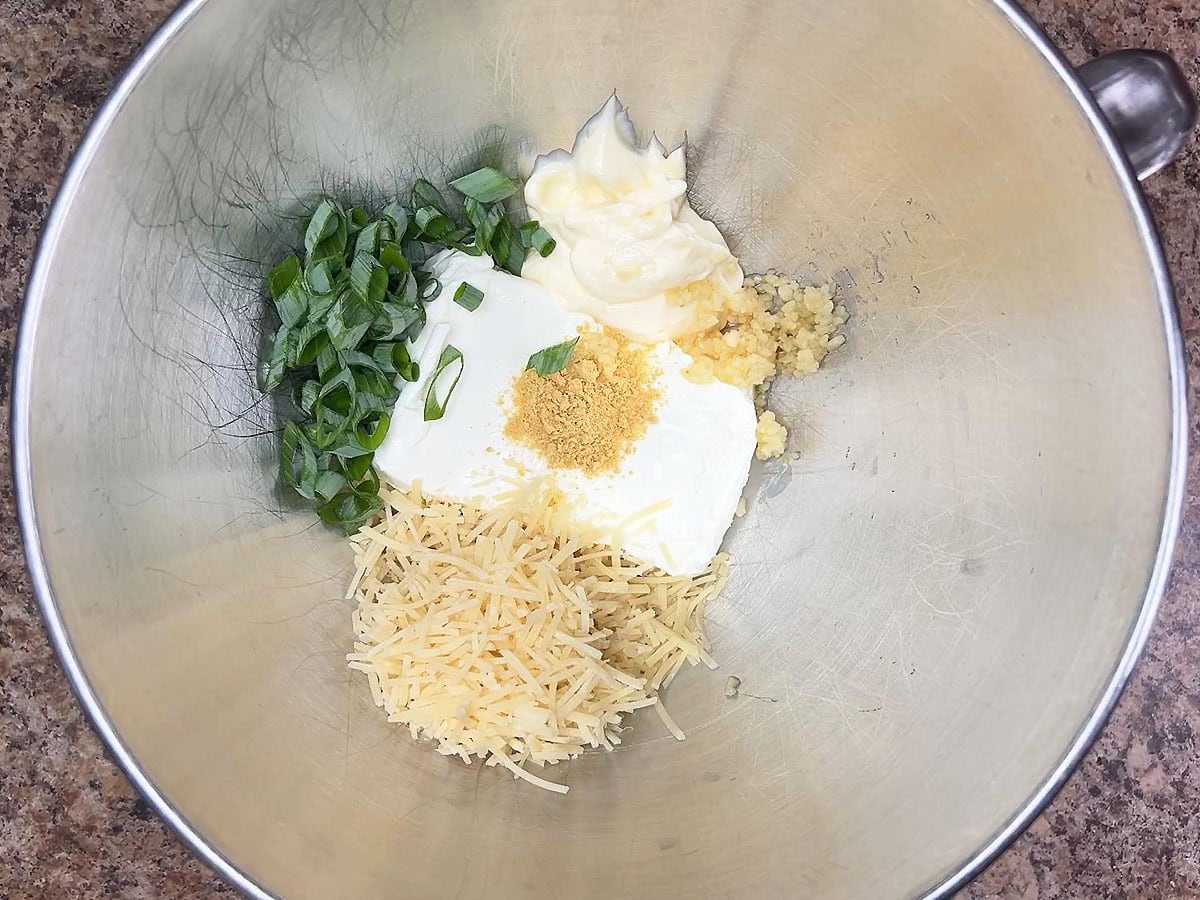 Eight ounces of cream cheese, ¾ cup of shredded Parmesan cheese, mayonnaise, dried mustard, green onions, and minced garlic in a mixing bowl.