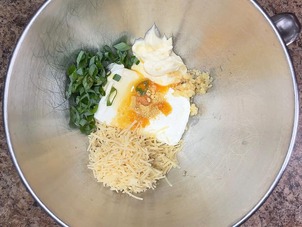 Eight ounces of cream cheese, ¾ cup of shredded Parmesan cheese, mayonnaise, dried mustard, green onions, minced garlic, and crab boil in a mixing bowl.