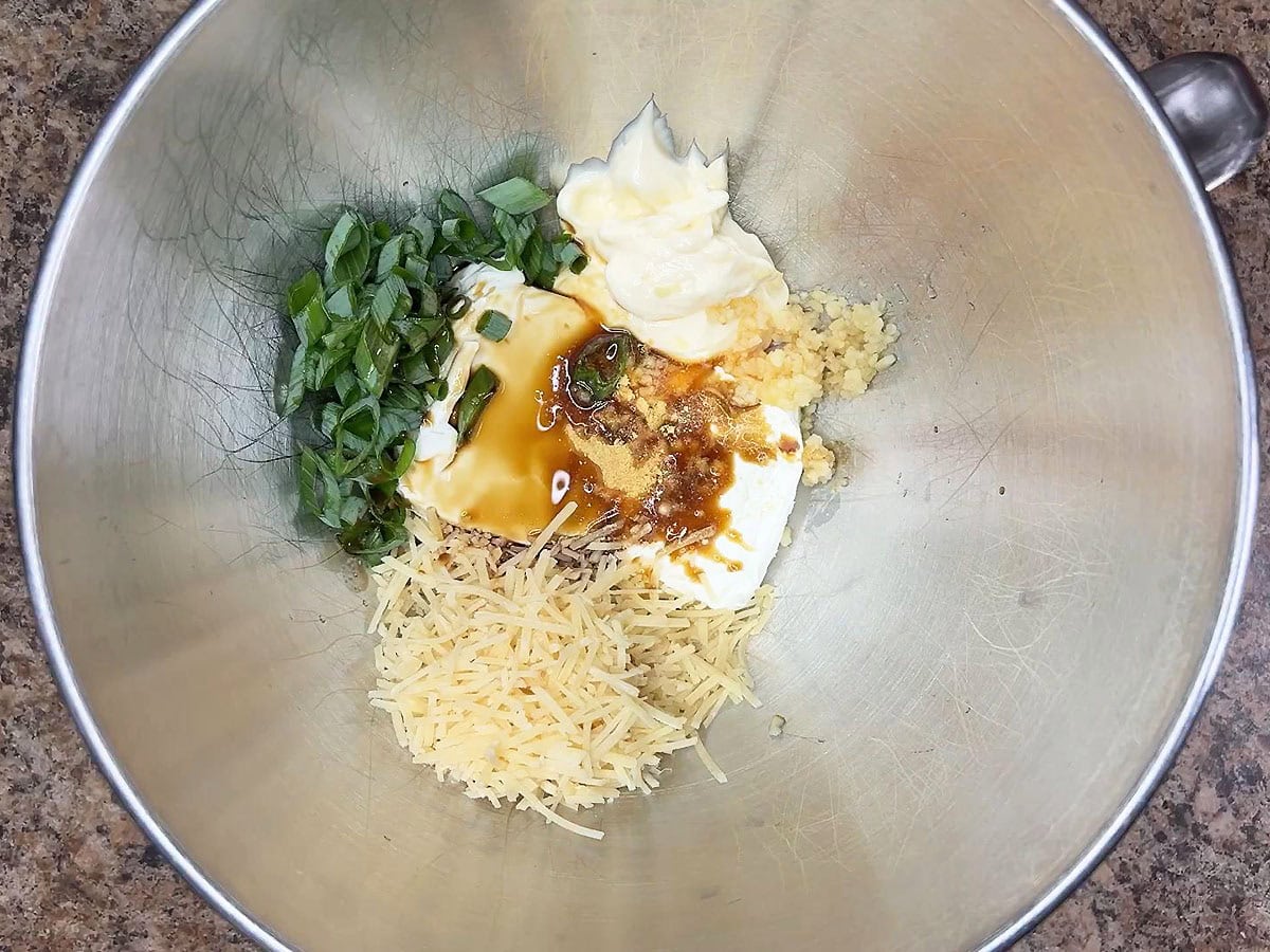 Eight ounces of cream cheese, ¾ cup of shredded Parmesan cheese, mayonnaise, dried mustard, green onions, minced garlic, crab boil, and Worcestershire sauce in a mixing bowl.