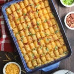 Bacon chicken ranch tater tot casserole garnished with sliced green onions, with small dishes of additional green onions, bacon bits and shredded cheese on the side.