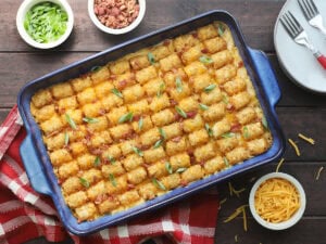 Bacon chicken ranch tater tot casserole garnished with sliced green onions, with small dishes of additional green onions, bacon bits and shredded cheese on the side.