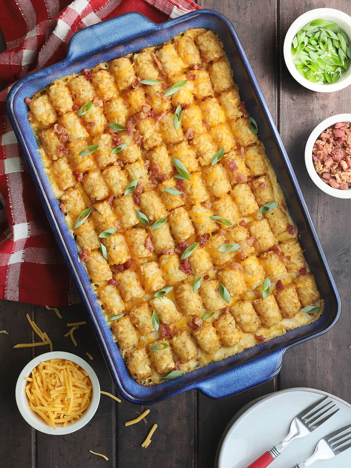 Bacon chicken ranch tater tot casserole garnished with sliced green onions, with small dishes of additional green onions, bacon bits and shredded cheese on the side.